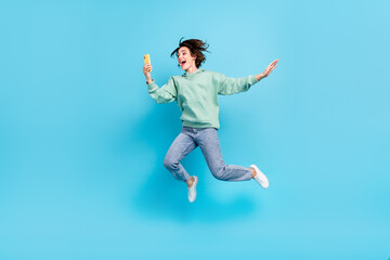Obraz premium Full size photo of sweet millennial brunette lady jump look telephone wear pullover jeans footwear isolated on blue background