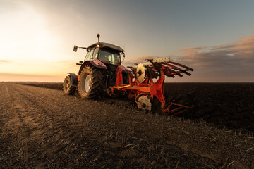 Obraz premium Tractor on the field during sunset.