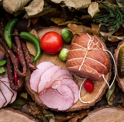 smoked ham, bacon and sausages on a wooden board of tree trunk