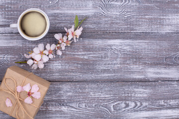 Spring composition with coffee, a gift wrapped in craft paper, spring blossoming almond branches with flowers on a gray shabby wooden table. Flat lay, copy space