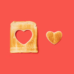 Unconditional love concept made of one slice of toasted bread with a heart shaped beside it. Flat lay arrangement with red background.