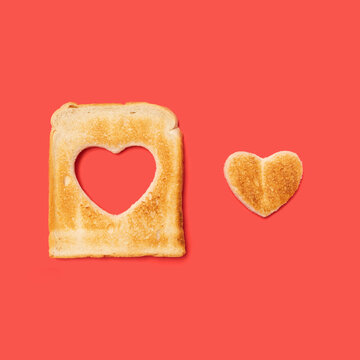 Unconditional love concept made of one slice of toasted bread with a heart shaped beside it. Flat lay arrangement with red background.