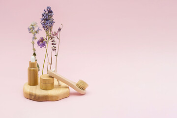 Bamboo jar, essential oil bottle with pipette, natural dry face brush on wooden podium, dried flowers, pastel pink background. Organic spa cosmetic beauty product, detoxing skin ritual.