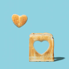 Minimal, love is in the air concept. Slice of toasted bread with a heart shape inside of it and little heart shaped toast levitating beside it. Aqua blue background.