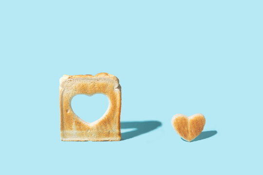 Love concept. Minimal arrangement made of slice of toasted bread with a heart shape inside of it and little heart shaped toast beside it. Bright blue background