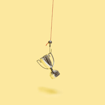 Minimal concept out of hook. Arrangement made of shiny trophy on a fish hook. Pastel yellow background.