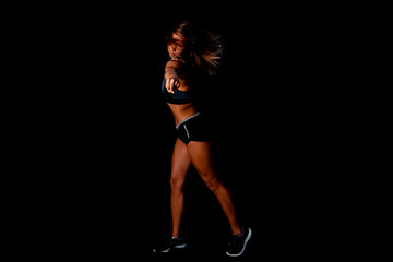 Fototapeta premium Beautiful athletic woman showing muscles on dark background. Slim tanned woman's body over black wall.