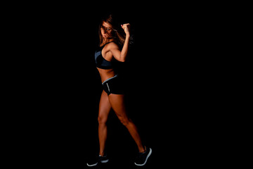 Fototapeta na wymiar Beautiful athletic woman showing muscles on dark background. Slim tanned woman's body over black wall.
