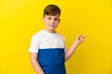 Little redhead boy isolated on yellow background pointing finger to the side