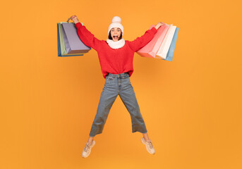 Big sales concept. Joyful shopaholic lady jumping with shopping bags, wearing knitted hat and...