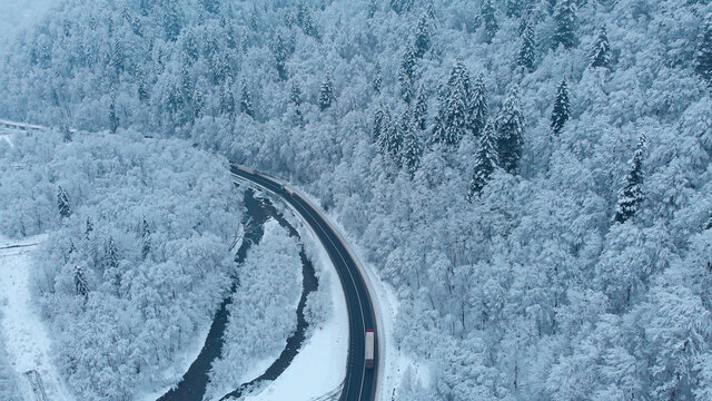 Aerial shot: Trucks driving by the road in winter forest.