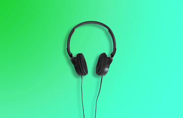 Computer headphones. Black headphones on a green  background. The concept of listening to music, creating audio, music. Computer work, abstraction and minimalist style.