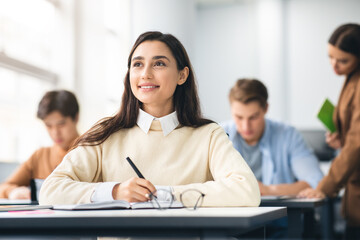 Smiling student sitting at desk in classroom thinking