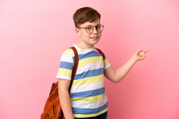Little redhead caucasian boy isolated on pink background pointing finger to the side