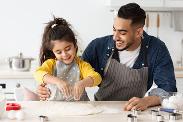 Cheerful arab dad and little daughter baking together in kitchen, making pizza
