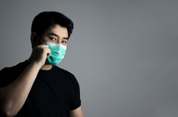 Young Asian man wearing a mask on a gray background. Concept of health care and self-protection from covid19 virus. with copy space.
