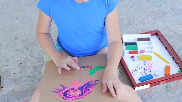 On-line training in creativity, the child sculpts on the street. The child sculpts a picture from plasticine, which depicts a multi-colored mermaid.