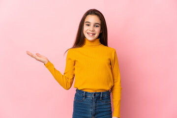 Little girl isolated on pink background holding copyspace imaginary on the palm to insert an ad