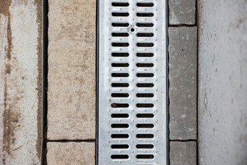 grate of storm sewer system in the middle of paving slabs. Aligned manhole cover