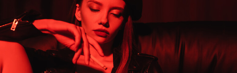 young sensual woman smoking in red light on black background, banner.