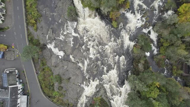 Aerial Drone Footage Above A Fast Flowing Water And River Rapids At The Falls Of Dochart In Killin, Trossachs National Park, Scotland With White Water, Rocks, A Village And Surrounded By Native Trees