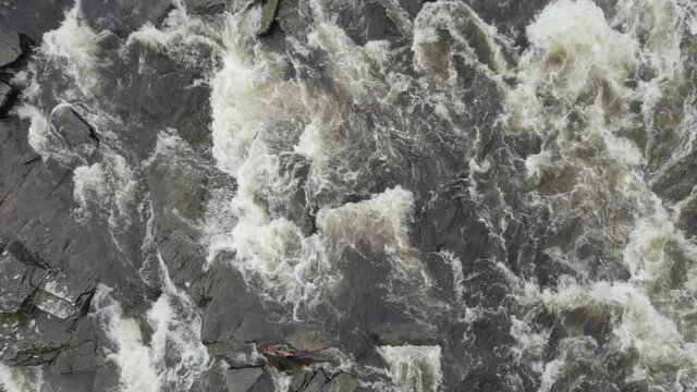 Aerial drone footage rising slowly over fast flowing water and river rapids at the Falls of Dochart in Killin, Trossachs National Park, Scotland with white water, rocks and surrounded by native trees.