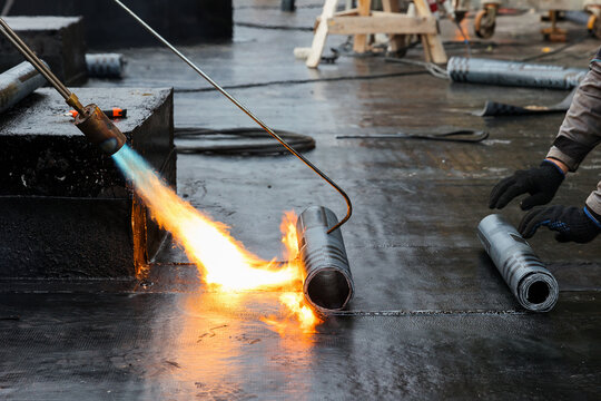 Flat roof installation with propane blowtorch during construction works with roofing felt. Heating and melting bitumen roofing felt. Roofer working tool. Waterproofing of modern buildings