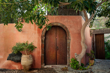 terracotta clay wall with brown arched door among greenery