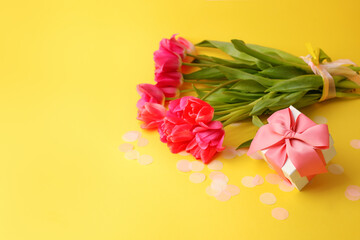 Pink red tulips bouquet, wrapped with ribbon and gift box overbright yellow background. Copy space. Happy Easter, 8 march, Woman day, Saint Valentine, Birthday, Mom day, banner