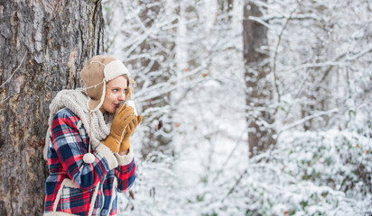 Fototapeta na wymiar woman winter drink. Girl enjoy snow fall. woman in mittens and hat drinking tea in snowy forest. outdoors on frosty day. travel and hiking. girl hiker drink cup of hot tea. warm yourself up