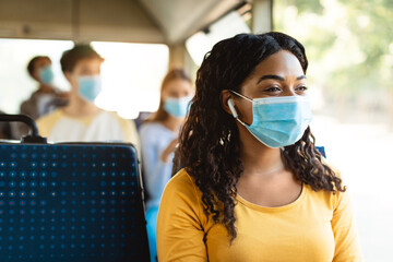 Black woman in mask listening to music going by autobus © Prostock-studio