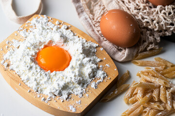 Macaroni penne, eggs and wheat flour with eco net bag on kitchen table. Ingredients for cooking Italian pasta.