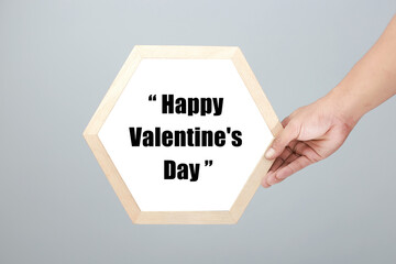 Male hand holding a hexagonal frame that says Happy Valentine's Day on a gray background