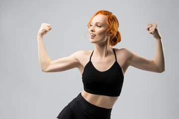 Positive young sportswoman showing biceps and smiling in studio