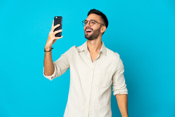 Young caucasian man isolated on blue background making a selfie