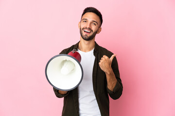 Young caucasian man isolated on pink background shouting through a megaphone and pointing side