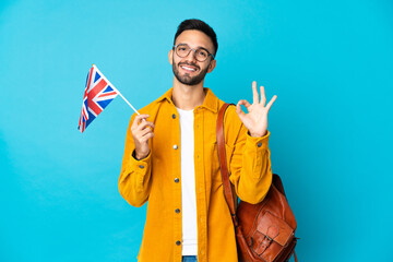Young caucasian man holding an United Kingdom flag isolated on yellow background showing ok sign...