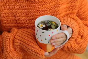 Hot herbal tea in a cup in a woman's hands. Warm up with hot tea during the cold season.