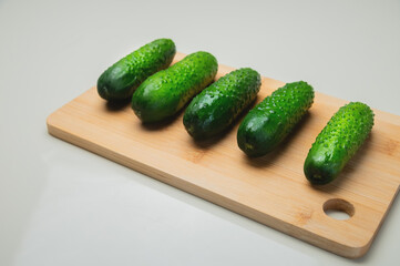 Close-up of several fresh cucumbers lie on a wooden cutting board on a white table. copy space vegetarian food