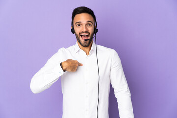 Telemarketer man working with a headset isolated on purple background with surprise facial expression