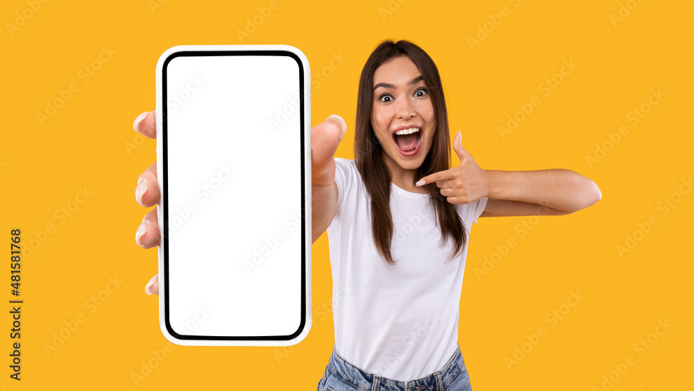 Wall mural excited woman showing white empty smartphone screen and pointing