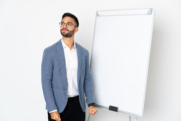 Young caucasian man isolated on white background giving a presentation on white board and looking up while smiling
