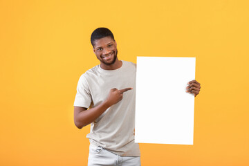 Free space for advertising. Excited black man pointing at blank poster with mockup for your design, yellow background