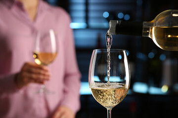 Pouring white wine from bottle into glass in bar, closeup. Space for text