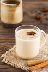 Homemade masala tea with milk and spices in a mug on a wooden table. Lactose free, vegan.