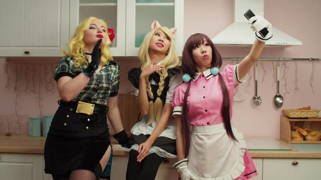 Joyful charming diverse multiethnic female cosplayers dressed in wigs and manga style costumes taking selfie shot on smartphone, making funny faces and gestures while relaxing at cosplay party.
