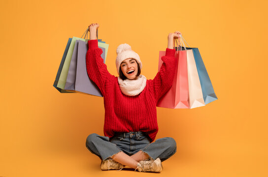 Seasonal sales. Happy woman holds shopping bags, sitting on yellow background and smiling to camera