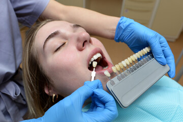 Close-up portrait of a young girl in a dental chair, check and choose the color of the teeth.