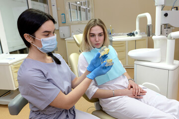Obraz premium attractive dentist in latex gloves holding teeth model near patient with clenched hands