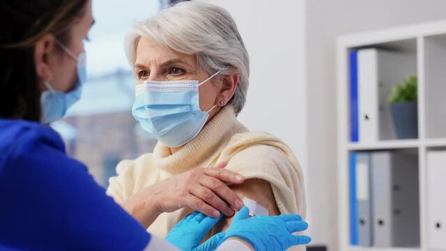 medicine, health and vaccination concept - doctor or nurse applying medical patch to vaccinated senior woman at hospital